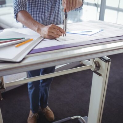 Osoba pracuje przy biurku z regulowanym stelażem do biurek, skupiona na rysunkach technicznych.