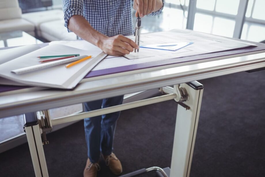 Osoba pracuje przy biurku z regulowanym stelażem do biurek, skupiona na rysunkach technicznych.