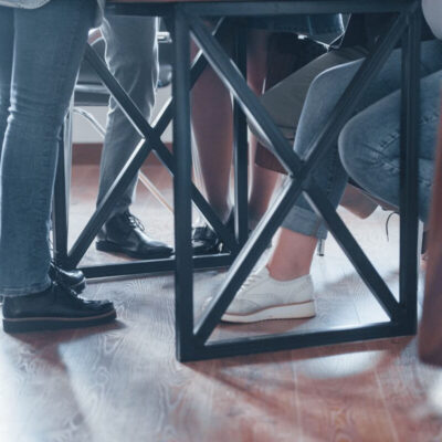 Grupa ludzi siedzi przy stole, pod którym widać składane stelaże do stołu.