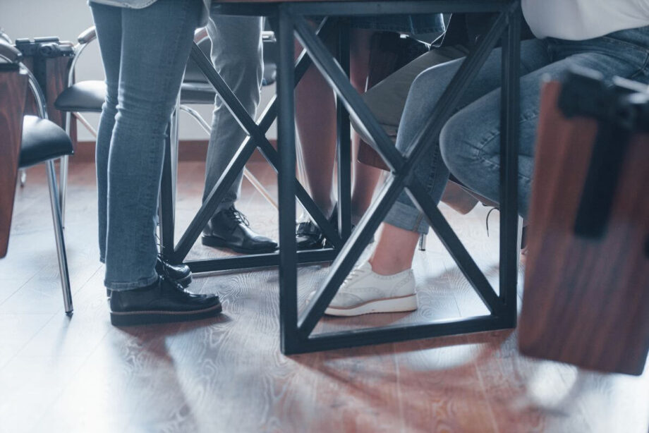 Grupa ludzi siedzi przy stole, pod którym widać składane stelaże do stołu.