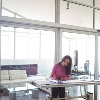 Kobieta pracująca przy dużym stole w przestrzeni biurowej, gdzie używane są stelaże do biurek open space.