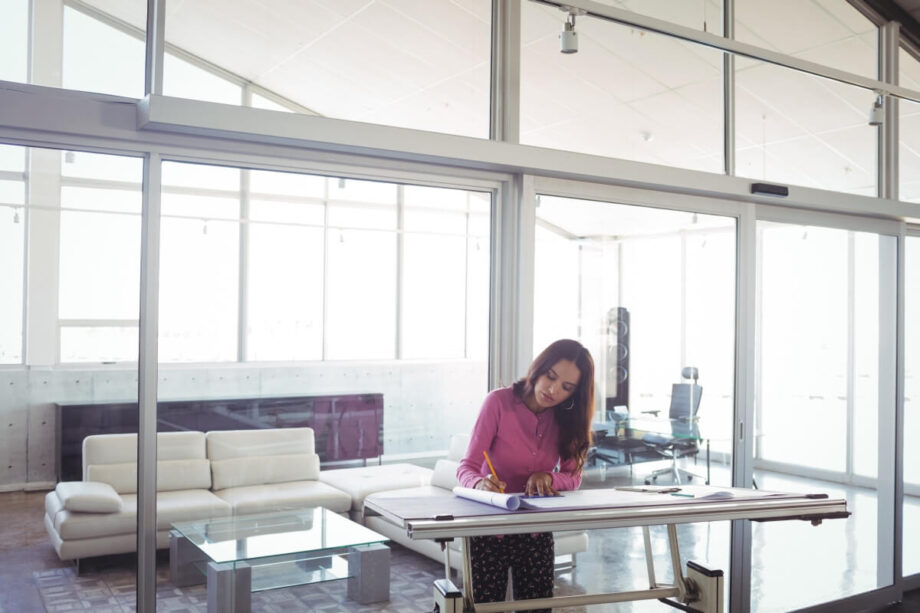 Kobieta pracująca przy dużym stole w przestrzeni biurowej, gdzie używane są stelaże do biurek open space.