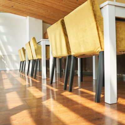 Jasne wnętrze z drewnianą podłogą i stelazami meblowymi wspierającymi żółte krzesła oraz białe stoły.