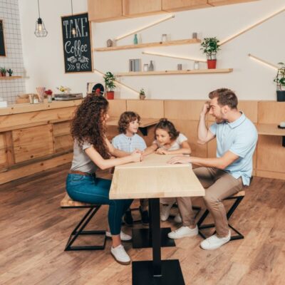 Rodzina siedzi przy stole w kawiarni, otoczona przez drewniane stelaze meblowe.