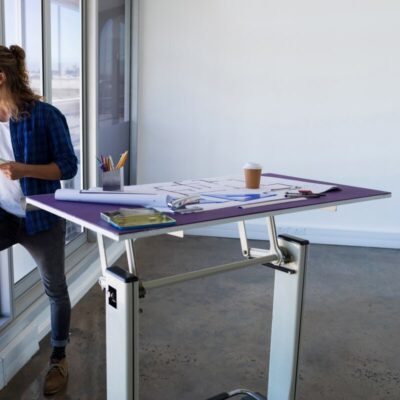 Mężczyzna patrzy przez okno obok biurka z planami, które ma stelaze regulowane.