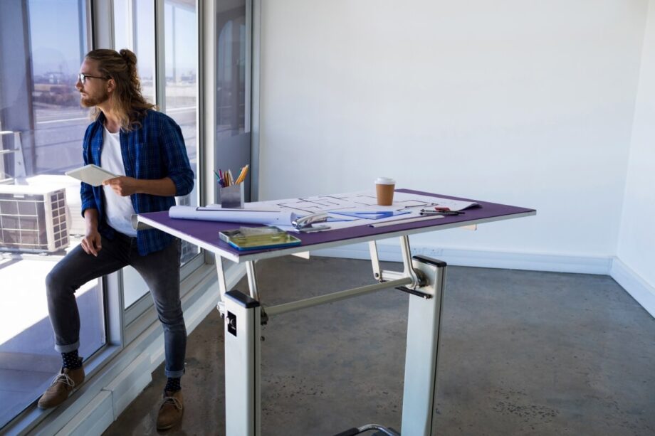 Mężczyzna patrzy przez okno obok biurka z planami, które ma stelaze regulowane.