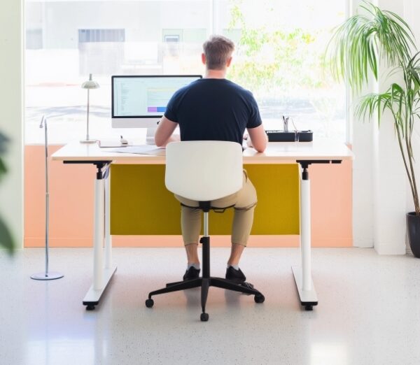 Mężczyzna pracuje przy biurku opartym na stelazach regulowanych.