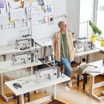 Kobieta w pracowni krawieckiej z maszynami do szycia ustawionymi na stelazach regulowanych.