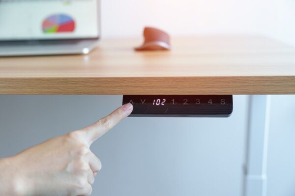 Osoba naciska przycisk na biurku z funkcją stelaze regulowane elektrycznie.