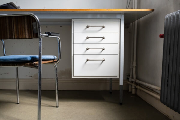 Biurko z białymi szufladami biurowymi i metalowym krzesłem obok.